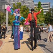 People in colorful costumes are dancing around a tree in an outdoor setting, cosplaying together.