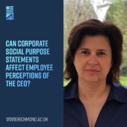A smiling person stands outdoors in front of a tree, holding a screenshot of a text-based corporate social purpose statement, questioning its effect on employee perceptions of the CEO.